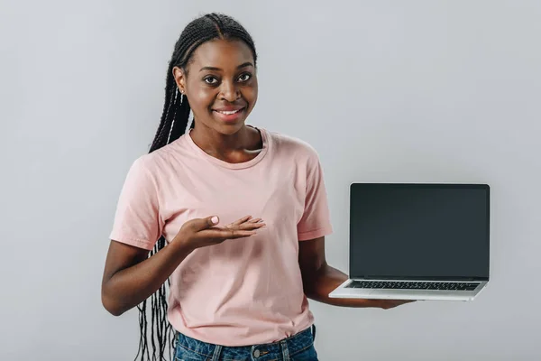 African American woman pointing with hand at laptop with blank screen and looking at camera isolated on grey — Stock Photo