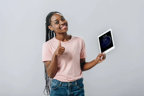 KYIV, UKRAINE - AUGUST 2, 2019: African American woman holding iPad with lock screen and showing thumb up isolated on grey — Stock Photo
