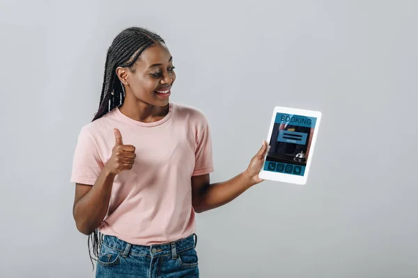 Afrikanerin hält digitales Tablet mit Buchungsanwendung in der Hand und zeigt Daumen nach oben isoliert auf grau — Stockfoto