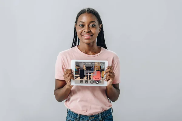Afrikanerin zeigt vor Kamera digitales Tablet mit Online-Buchungsanwendung isoliert auf grau — Stockfoto