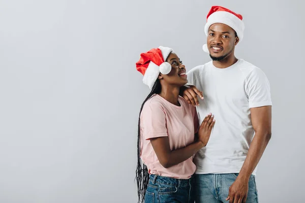 Афроамериканская пара в шляпах Санта-Клауса изолирована от серых — стоковое фото