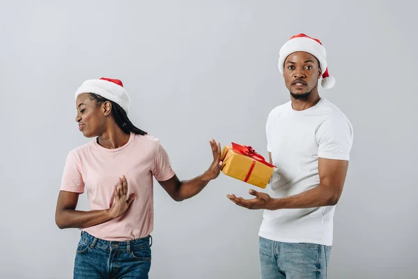 African American woman in Santa hat rejecting gift box from man isolated on grey — Stock Photo