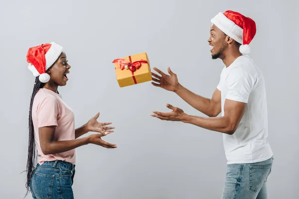 Afrikanisch-amerikanisches Paar mit Weihnachtsmannhut wirft Geschenkbox isoliert auf grau — Stockfoto