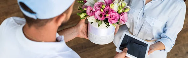 Plan panoramique de livraison homme donnant des fleurs et tablette numérique avec écran blanc à la femme — Photo de stock
