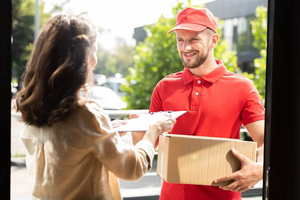 Femme donnant presse-papiers à heureux livreur homme avec boîte — Photo de stock