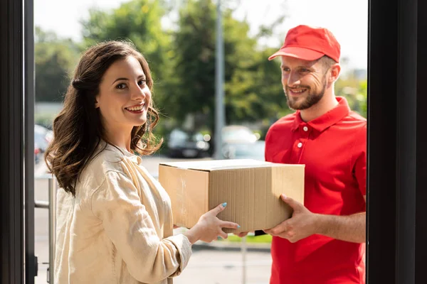 Mulher alegre sorrindo perto de homem de entrega feliz com caixa — Fotografia de Stock