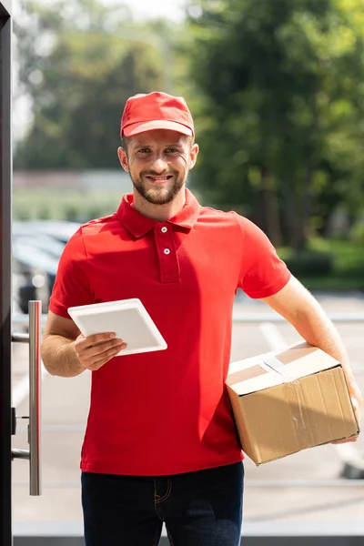 Happy delivery man holding box and digital tablet — Stock Photo