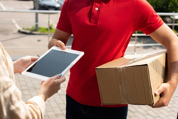 Vista ritagliata di consegna uomo tenendo pacchetto vicino alla donna con tablet digitale — Foto stock
