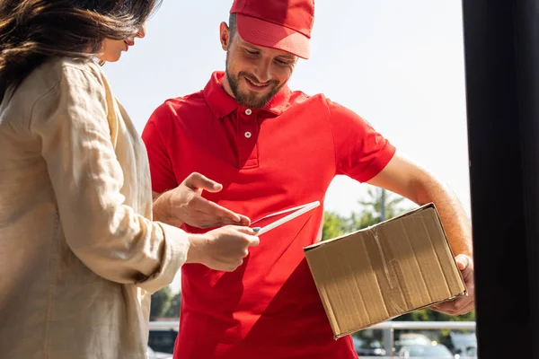 Cheerful delivery man gesturing while looking at digital tablet near woman — Stock Photo