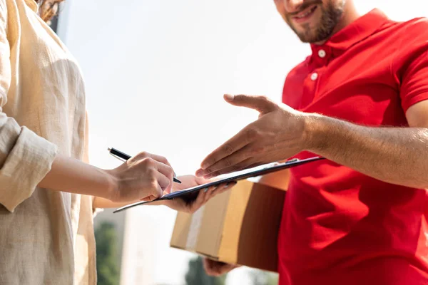 Cropped view of cheerful delivery man holding box and gesturing near clipboard and woman — Stock Photo