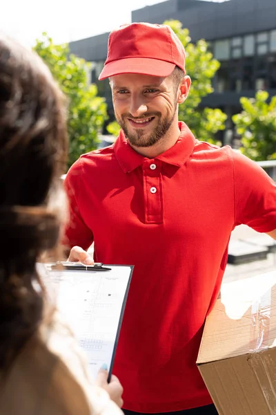 Selective focus of delivery man in cap holding box and looking at woman — Stock Photo