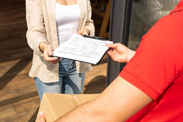 Cropped view of delivery man holding box and giving clipboard  to young woman — Stock Photo