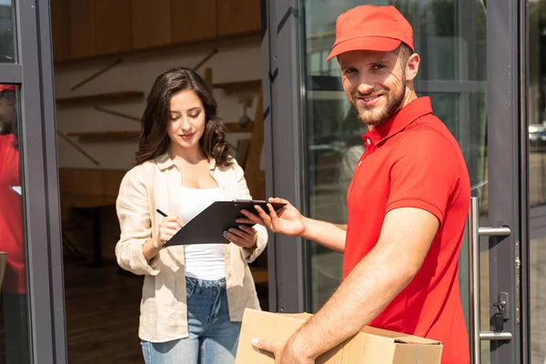 Beau livreur tenant presse-papiers près de fille attrayante — Photo de stock