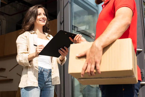 Recortado vista de entrega hombre celebración caja cerca atractiva chica con portapapeles - foto de stock