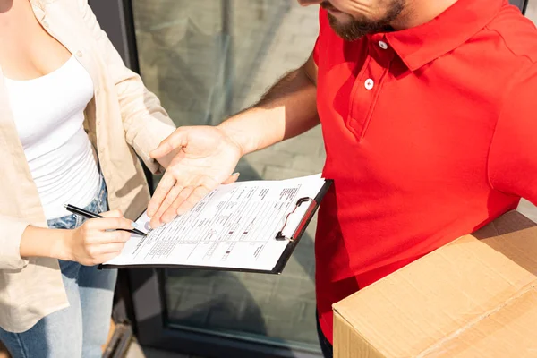 Cropped view of delivery man gesturing near clipboard in hands on woman — Stock Photo