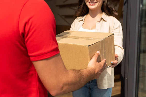 Vista recortada del repartidor hombre dando caja de cartón a la mujer feliz - foto de stock