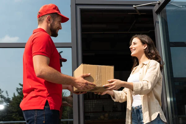 Guapo repartidor hombre dando caja de cartón a mujer alegre - foto de stock