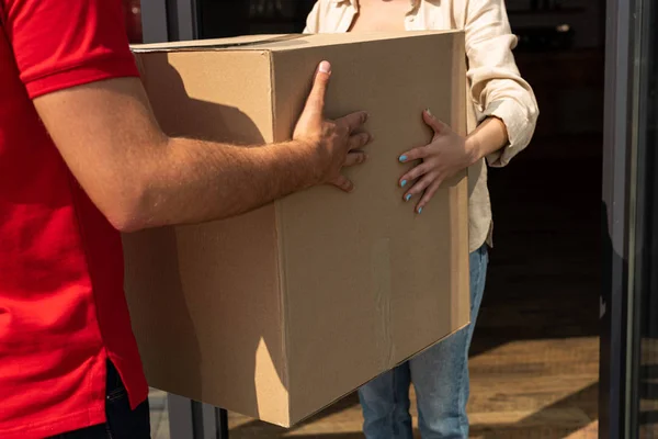 Vista recortada de repartidor hombre dando caja de cartón a mujer - foto de stock