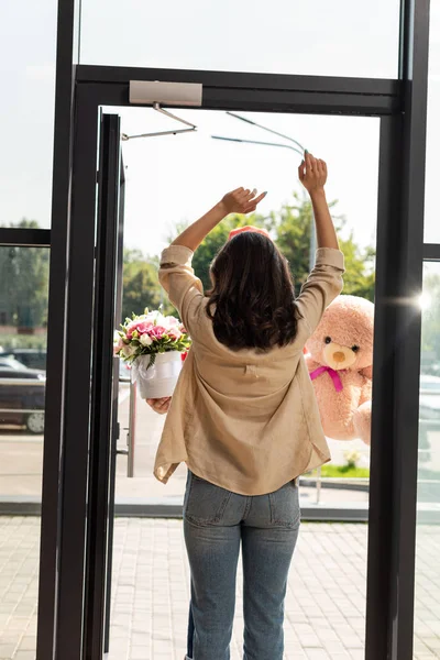 Back view of woman standing with hands above head near delivery man with gifts — Stock Photo