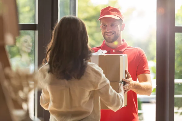 Rückseite der Frau, die Karton von glücklichem Zusteller erhält — Stockfoto