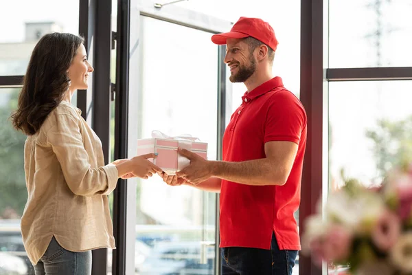 Foyer sélectif de beau livreur homme en chapeau donnant cadeau rose à la femme heureuse — Photo de stock