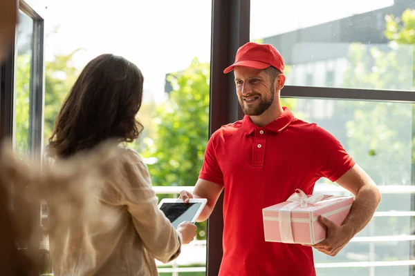 Foyer sélectif de livraison heureux homme tenant cadeau rose et donnant tablette numérique à la femme — Photo de stock