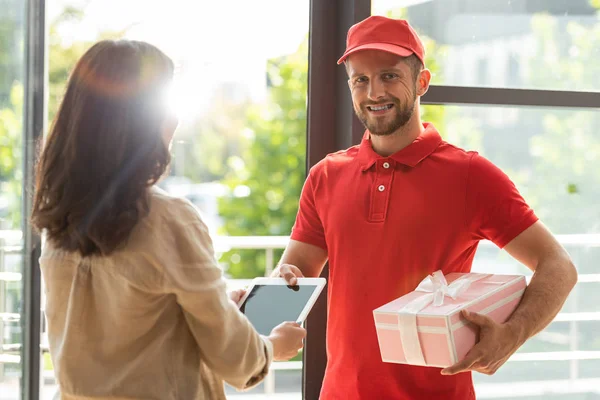Happy bearded delivery man holding pink present near woman with digital tablet — Stock Photo