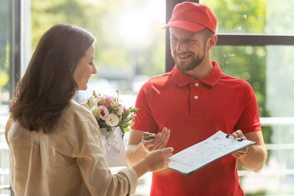 Bärtiger und glücklicher Zusteller mit Klemmbrett und Stift in der Nähe der schönen Frau — Stockfoto