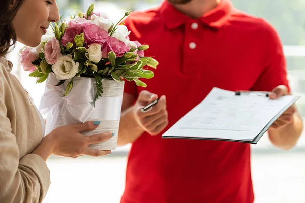 Vue recadrée de livraison homme tenant presse-papiers près de la femme avec des fleurs — Photo de stock