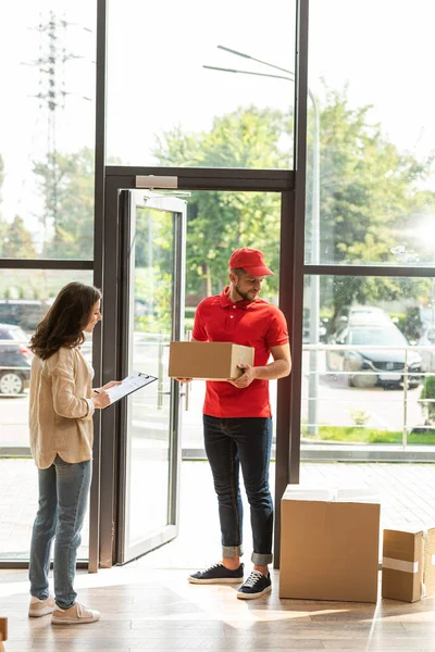 Femme signature papier sur presse-papiers près de livraison homme et boîtes — Photo de stock