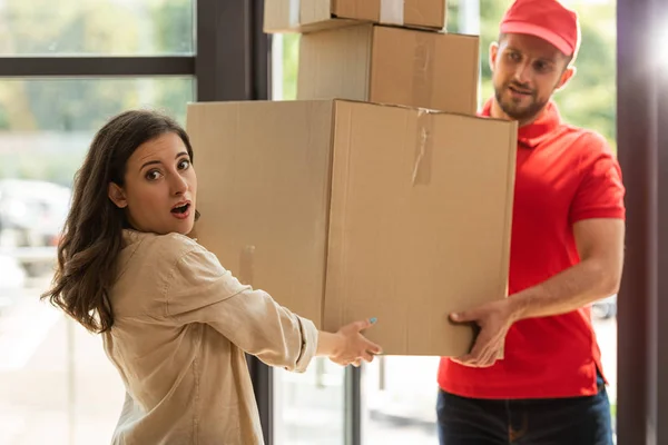 Selective focus of surprised girl taking carton boxes near delivery man — Stock Photo