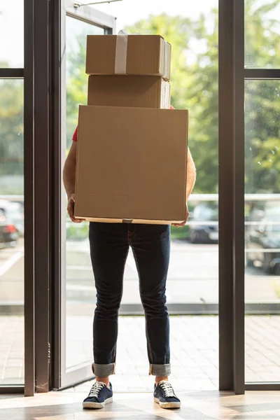 Livreur couvrant le visage tout en tenant debout et boîtes en carton — Photo de stock