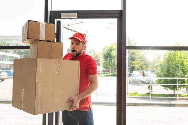 Shocked and bearded man holding carton boxes while looking at camera — Stock Photo