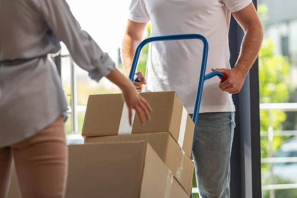 Vue recadrée du livreur tenant le chariot de livraison avec des boîtes près de la femme — Photo de stock