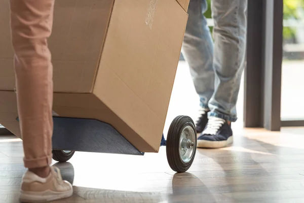 Vue recadrée du livreur tenant chariot de livraison avec boîte près de la fille — Photo de stock