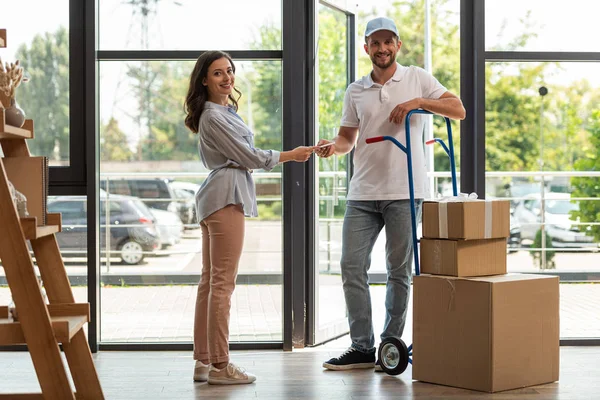 Selective focus of delivery man standing near delivery cart with boxes and woman with digital tablet — Stock Photo