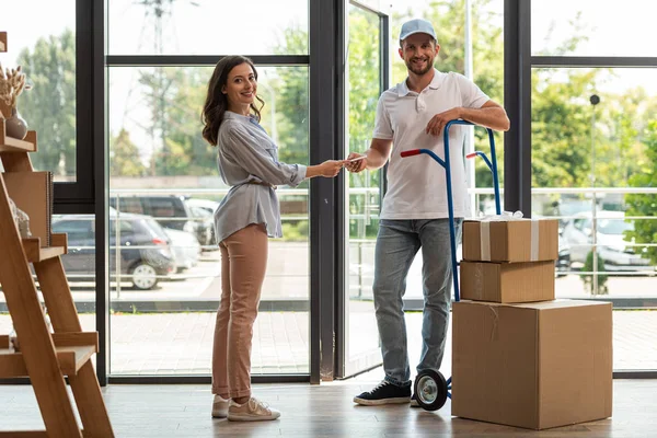 Foyer sélectif de livraison homme debout près du chariot de livraison avec des boîtes et femme avec tablette numérique — Photo de stock