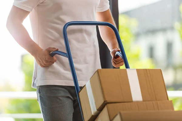 Vista recortada del hombre de entrega que sostiene el carro de entrega con cajas de cartón - foto de stock