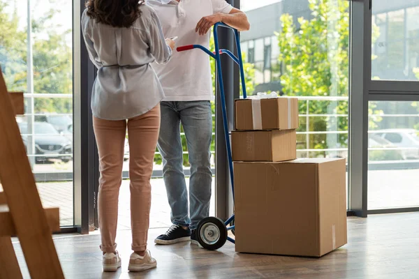 Back view of woman holding digital tablet near delivery man standing near delivery cart with boxes — Stock Photo