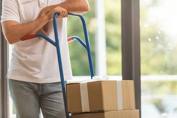 Vista recortada del hombre de entrega de pie cerca del carrito de entrega con cajas de cartón - foto de stock