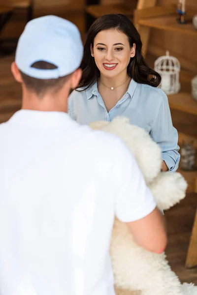 Rückansicht des Lieferanten mit Teddybär in der Nähe der attraktiven Frau — Stockfoto