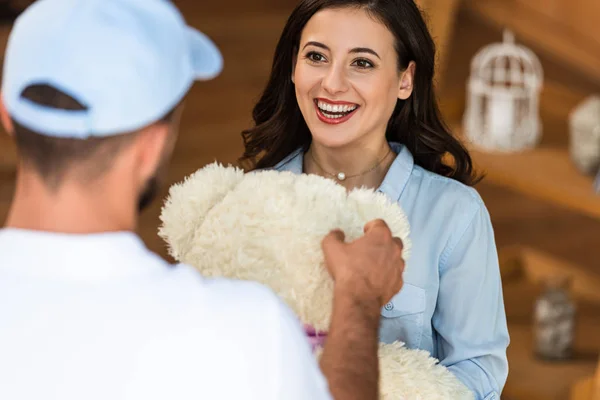 Enfoque selectivo de la mujer feliz mirando al repartidor hombre con oso de peluche - foto de stock