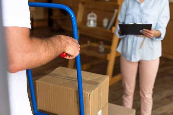 Selective focus of delivery man holding delivery cart with boxes near woman — Stock Photo