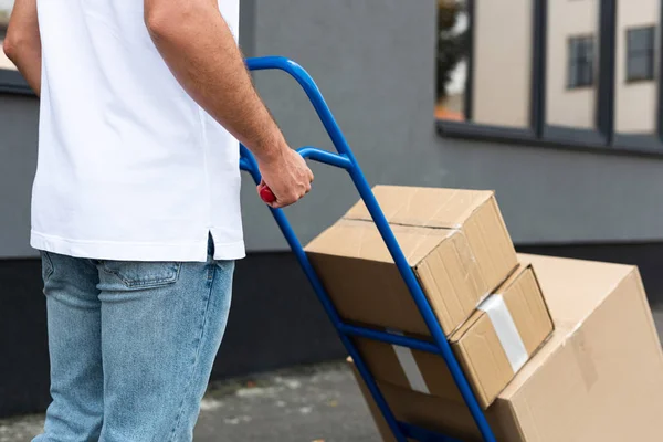 Vista recortada del repartidor de pie con carro de reparto cerca del edificio — Stock Photo