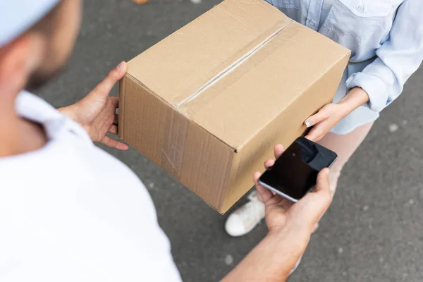 Overhead view of delivery man giving box to woman while taking smartphone with blank screen outside — Stock Photo