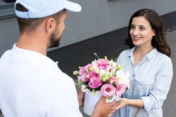 Selective focus of cheerful girl receiving flowers from delivery man outside — Stock Photo