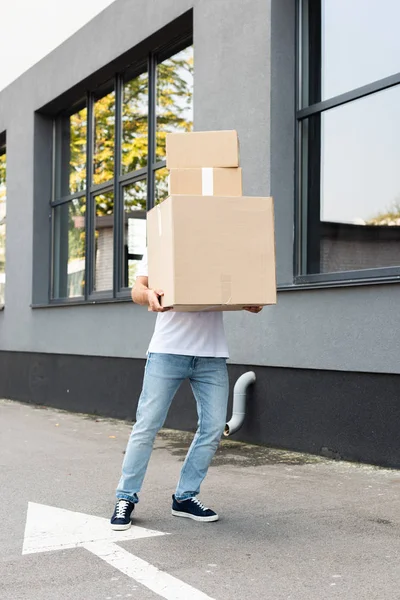 Repartidor cubriendo la cara mientras sostiene paquetes cerca del edificio - foto de stock