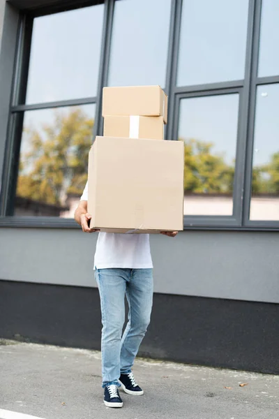 Курьер прикрывает лицо, держа коробки возле здания — стоковое фото