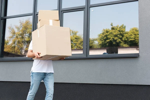 Delivery man in denim blue jeans holding boxes near building — Stock Photo