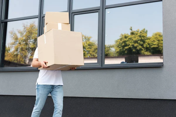 Homem de entrega em jeans jeans azul jeans segurando caixas perto do edifício — Fotografia de Stock